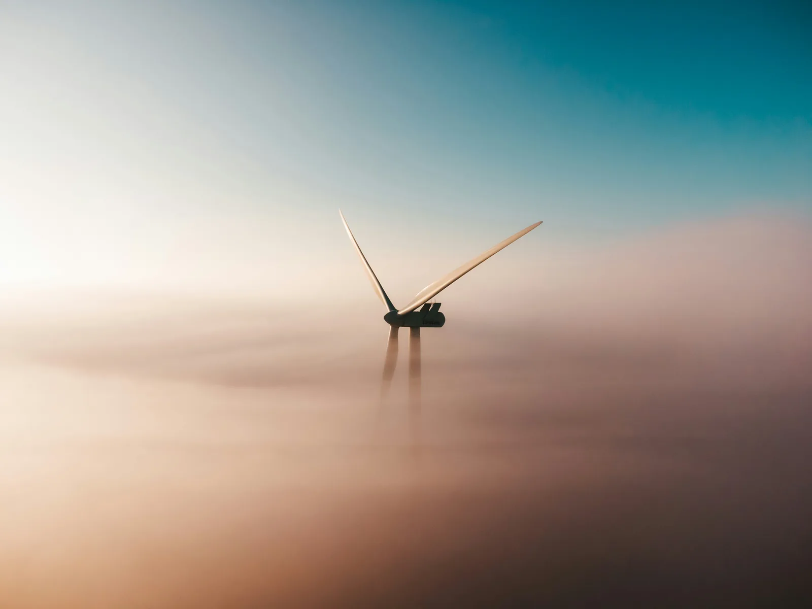 Aerogenerador que asoma sobre una capa de niebla bajo un cielo azul turquesa